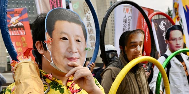 A man (L) wearing a face mask with the image of China's President Xi Jinping joins other human rights activists holding Olympic Rings as they protest in Taipei against the 2022 Beijing Olympic Games to mark Human Rights Day on December 10, 2021. (Photo by Sam Yeh / AFP) (Photo by SAM YEH/AFP via Getty Images)