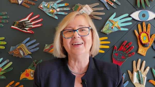 Krystyna Kacpura stands against a wall decorated with colourful hands