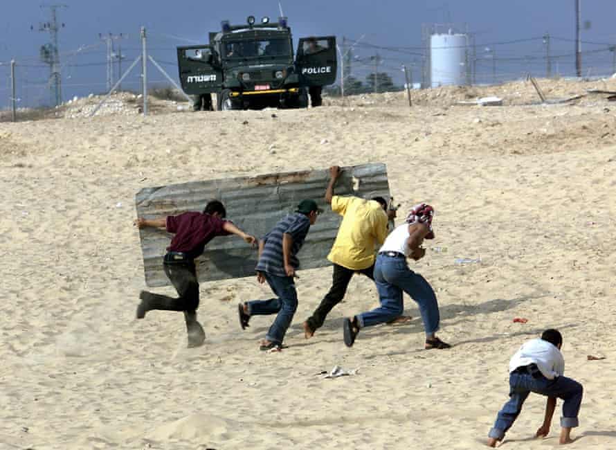 Palestinian youths take cover from police behind a sheet of corrugated iron in 2000