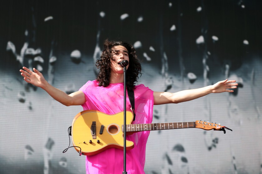 A male singer in a pink dress performs onstage