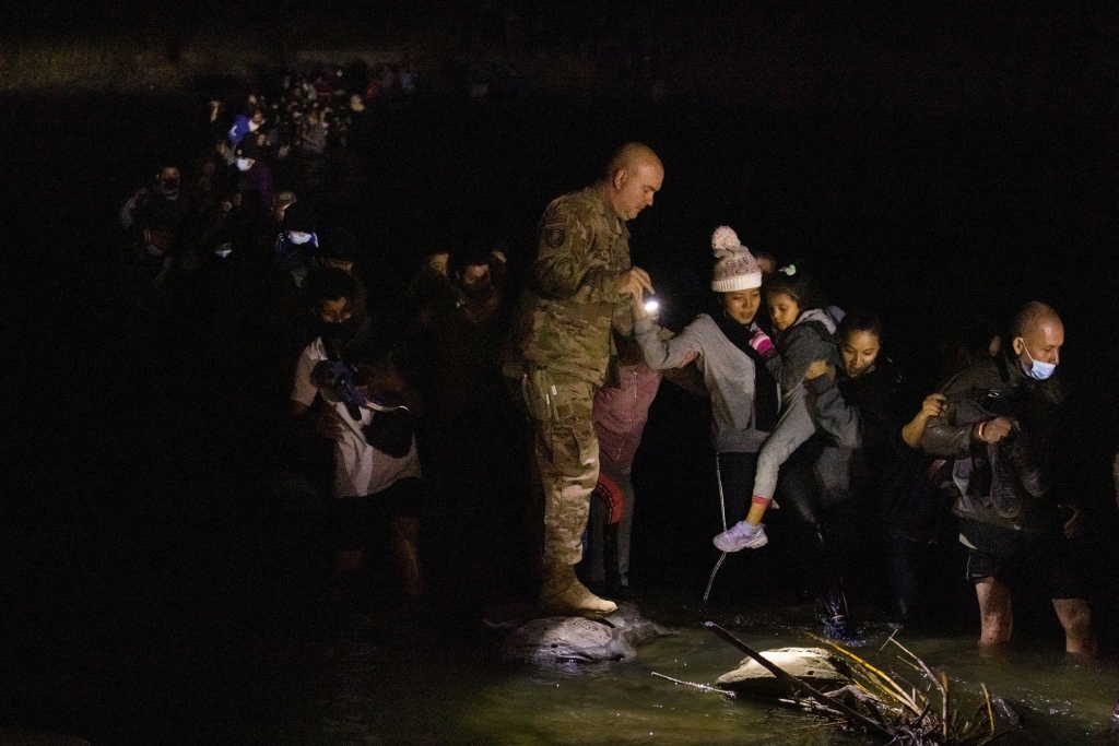 A member of the Texas Army National Guard lights the path as asylum-seeking migrants wade through the Rio Grande.
