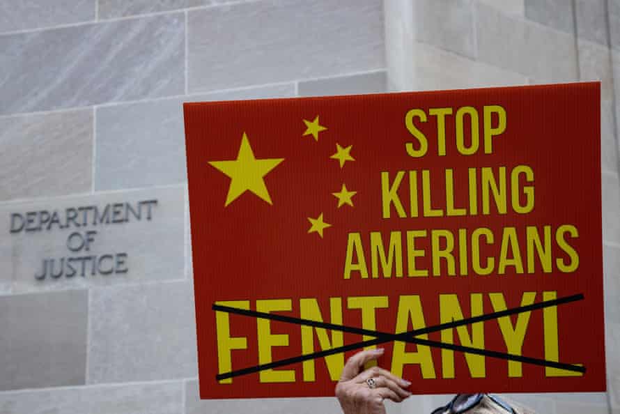 The hand of a demonstrator in front of the Department of Justice can be seen holding a sign reading ‘Stop killing Americans’ with the word ‘fentanyl’ below crossed out. 