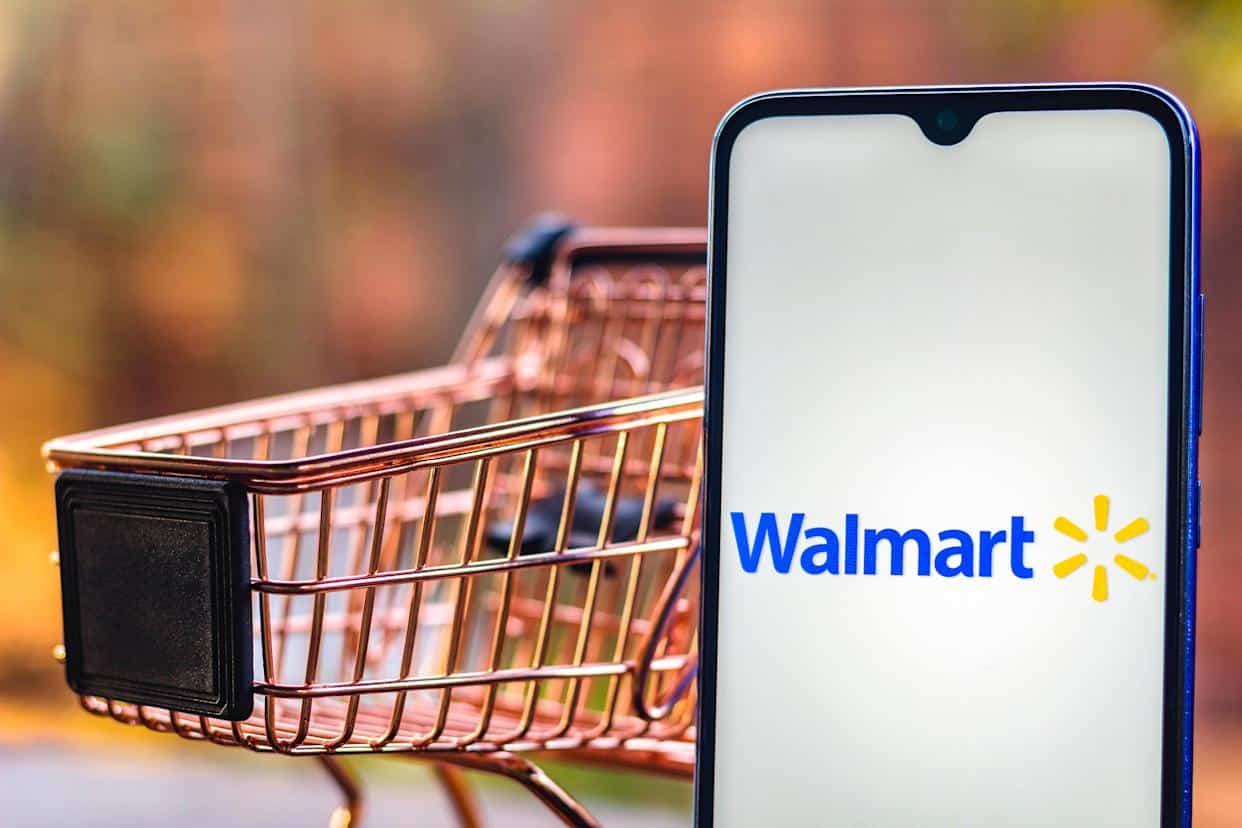Miniature shopping cart next to Smart phone showing Walmart logo.