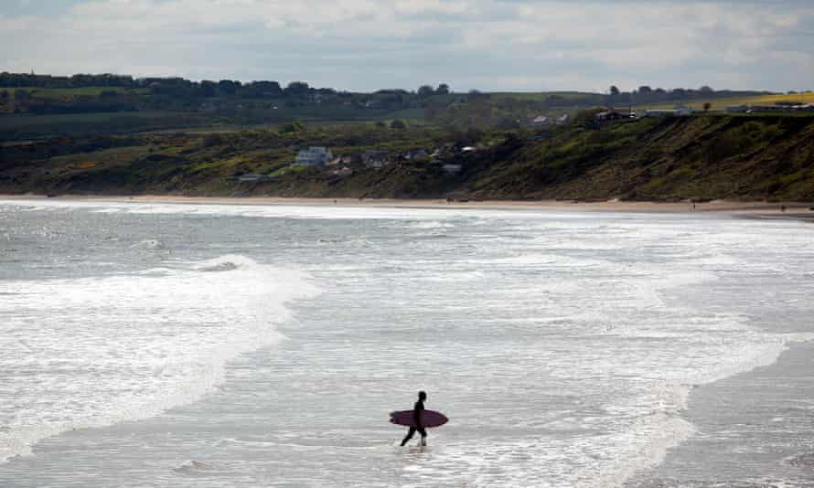 A surfer walks through the sea as he returns to the shoreline at Filey, North Yorkshire.